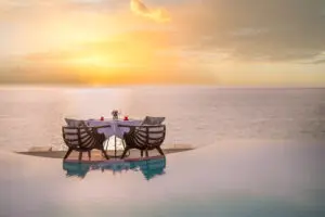 a table and chairs by a pool with a sunset in the background upmarket luxury travel