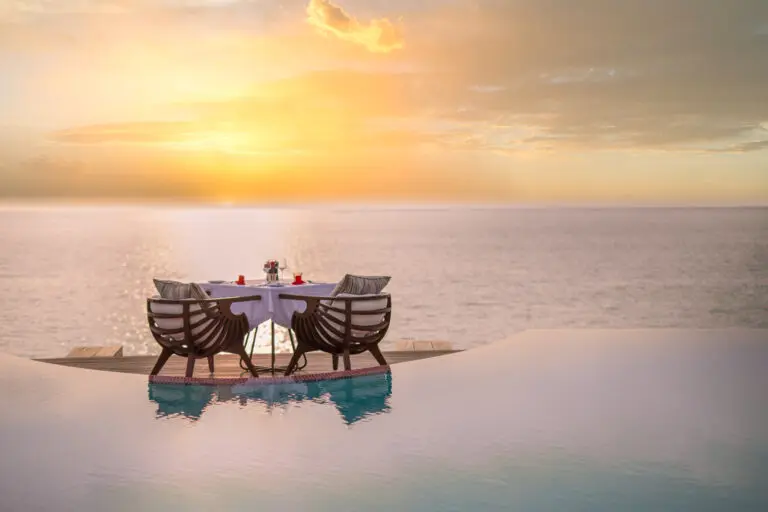 a table and chairs by a pool with a sunset in the background upmarket luxury travel